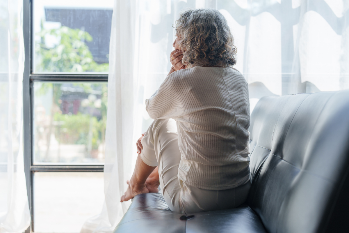 Women on couch with back turned looking out the window contemplating how religious triggers might still be affecting her