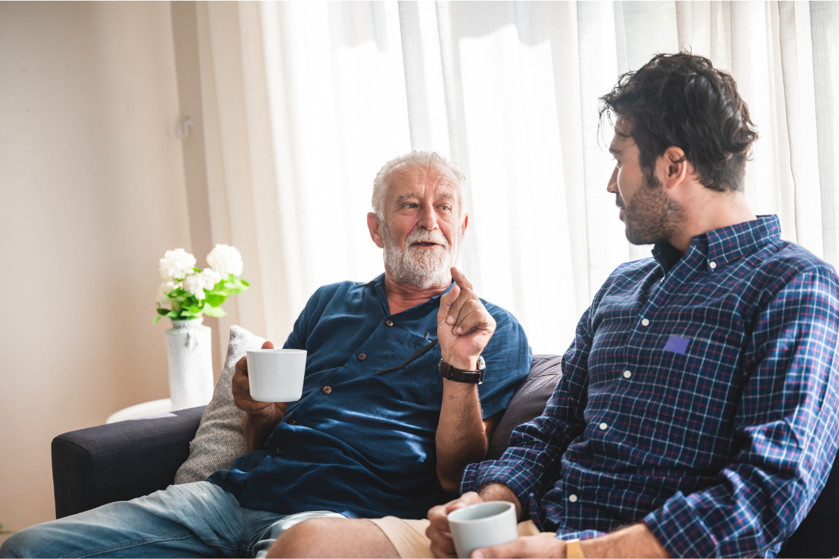 Older man talking to his son on the couch drinking coffee. Exploring how to untangle religious trauma from family trauma