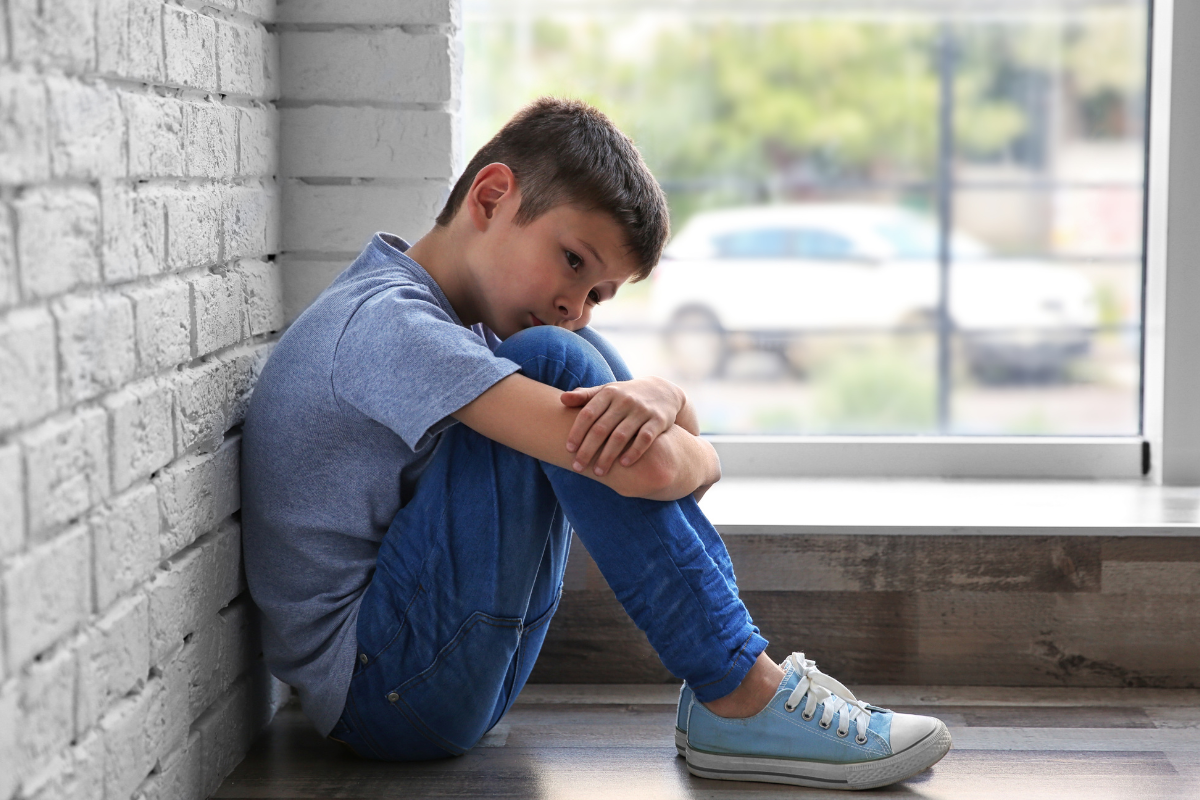 A child with face on knees who has experience religious authoritarian parenting.