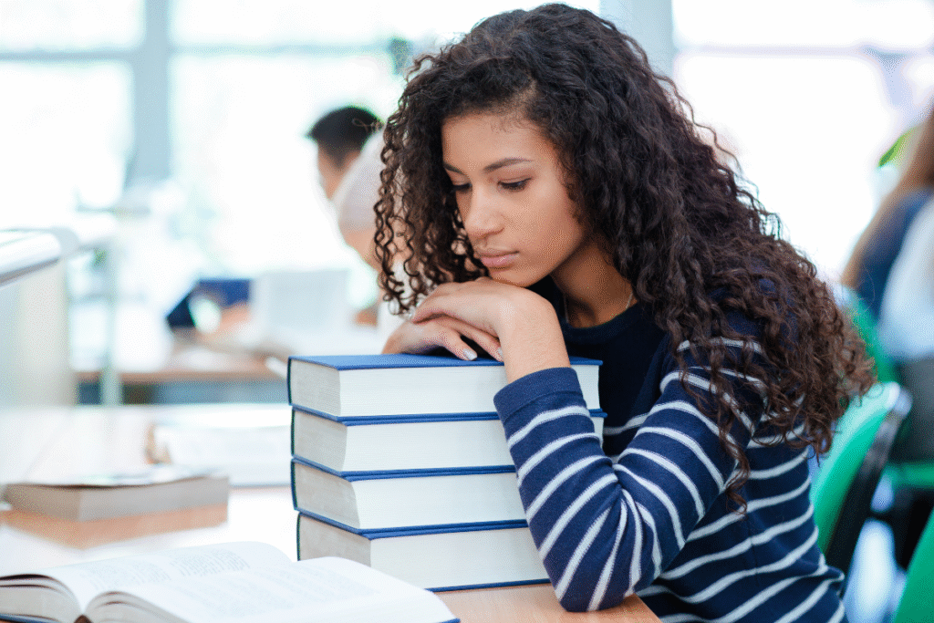 Girl with chin propped on hands on top of a pile of books looking dejected because her religious upbringing left her feeling starved for love