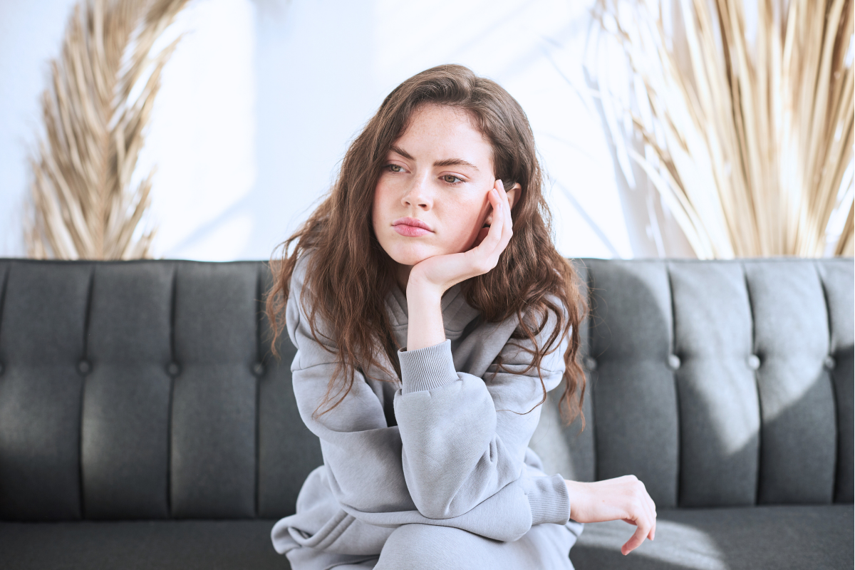 Woman on couch with face resting on hand experiencing anger as an outcome of religious trauma