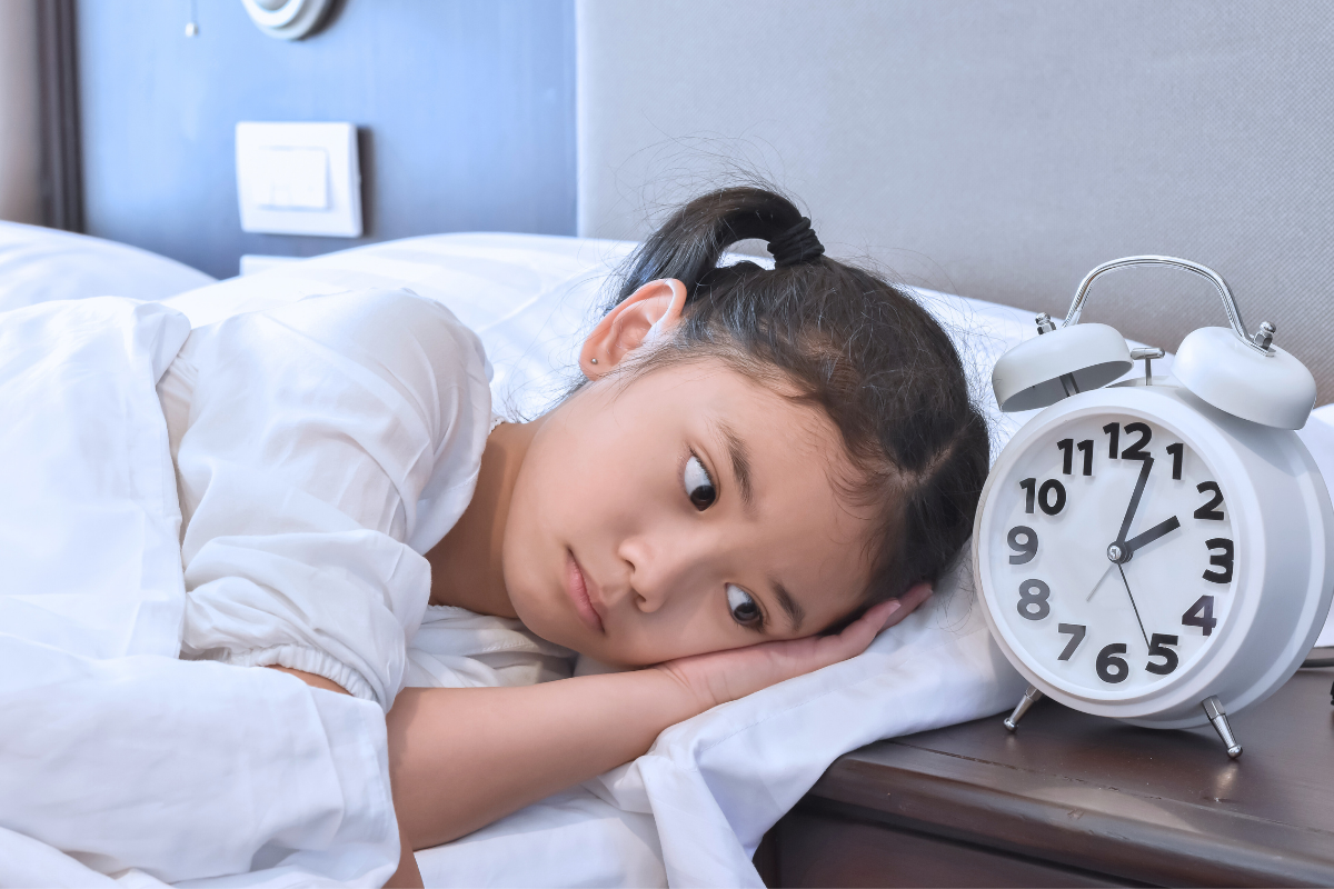 a girl lying on a bed with a white alarm clock