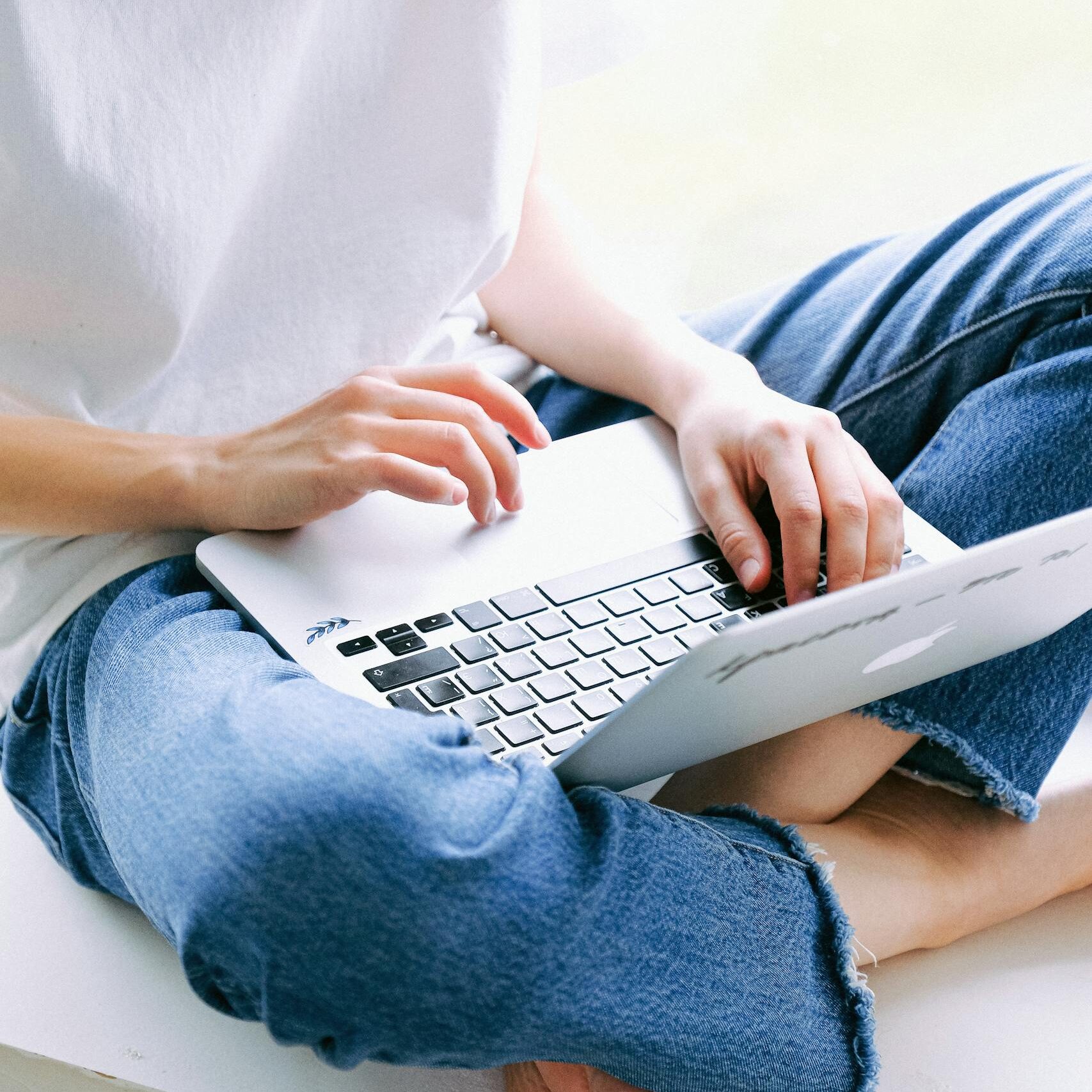 Woman sitting cross-legged in casual jeans working on a laptop indoors.